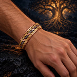 Elder Code bracelet with intertwined copper, gold and silver toned strands, worn on a hand model’s wrist against a dark blue and golden tree background.